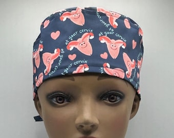 May include: A blue surgical scrub hat with a pink uterus graphic and the text "at your cervix" repeated throughout the design.