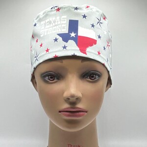 Peut inclure: Un bonnet de chirurgien bleu clair avec le drapeau de l'État du Texas et l'inscription "TEXAS STRONG". Le bonnet est orné d'étoiles rouges, blanches et bleues. Le bonnet est présenté sur une tête de mannequin.