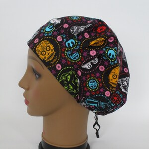 May include: A black skull cap with a colorful pattern of skulls, flowers, and other designs. The cap is on a mannequin head. The cap has a drawstring closure.