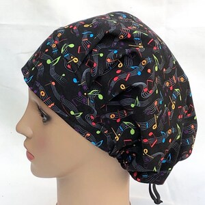 May include: Black scrub hat with a colorful musical notes pattern. The hat has a drawstring.