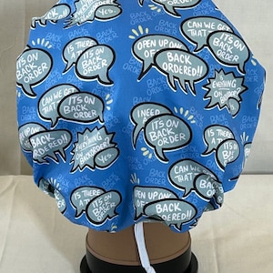 May include: A blue surgical scrub cap with a repeating pattern of speech bubbles. The speech bubbles contain phrases like "It's on back order" and "Can we get that?"