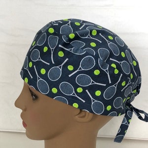May include: A blue scrub hat with a white tennis racket and green tennis ball pattern.