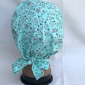 May include: A turquoise blue scrub hat with a repeating pattern of cartoon genie characters from the Disney movie Aladdin. The hat has a tie at the back.