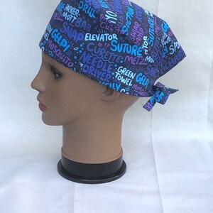 May include: A black scrub hat with a colorful print of medical terms and symbols. The hat has a tie on the back.
