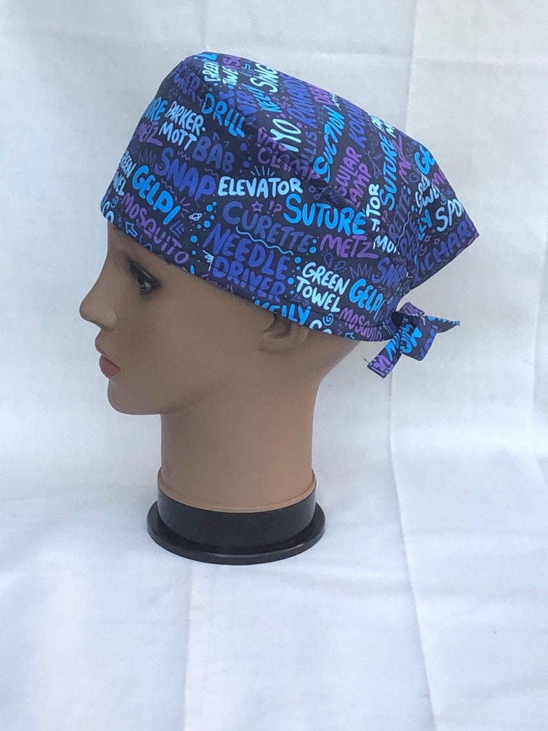 May include: A black scrub hat with a colorful print of medical terms and symbols. The hat has a tie on the back.