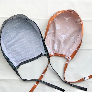 May include: Two fabric hats with ties. One hat is black with white text and the other is orange with white text and a white Longhorn steer logo.