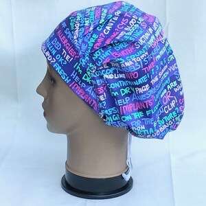May include: A purple, blue, pink and green patterned surgical scrub hat with a white drawstring. The hat has a variety of medical terms printed on it, including "allergies", "help", "implants", "anesthesia", "time", "dry page", "contaminate", "mid line", "birth", "blood", "cyst", "cauter", "pain", "clean", "nurse", "specimen", "dressing", "suction", "county", "ana", "stickers", "the stitch", "yuc", "who are you", "or", "what", "we", "for the next clip", "scrubbing", "cold", "partial suture", "on the floor", "wing", "implants", "fresh", "giled", "rilling ok", "bed tie", "not", "what", "is", "i'm", "the rogue", "were class", "pring", "live", "amold ro03", "bing & delu", "cure", "love".