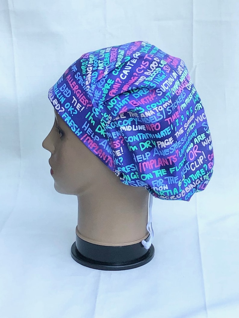 May include: A purple, blue, pink and green patterned surgical scrub hat with a white drawstring. The hat has a variety of medical terms printed on it, including "allergies", "help", "implants", "anesthesia", "time", "dry page", "contaminate", "mid line", "birth", "blood", "cyst", "cauter", "pain", "clean", "nurse", "specimen", "dressing", "suction", "county", "ana", "stickers", "the stitch", "yuc", "who are you", "or", "what", "we", "for the next clip", "scrubbing", "cold", "partial suture", "on the floor", "wing", "implants", "fresh", "giled", "rilling ok", "bed tie", "not", "what", "is", "i'm", "the rogue", "were class", "pring", "live", "amold ro03", "bing & delu", "cure", "love".