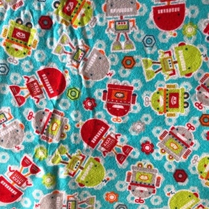 K&ouml;nnte beinhalten: Ein t&uuml;rkisfarbener Stoff mit einem sich wiederholenden Muster aus bunten Robotern. Die Roboter sind rot, gr&uuml;n, grau und orange, mit Details wie Antennen und Zahnr&auml;dern. Der Hintergrund umfasst wei&szlig;e Kreise, rote Blumen und graue Sechsecke.