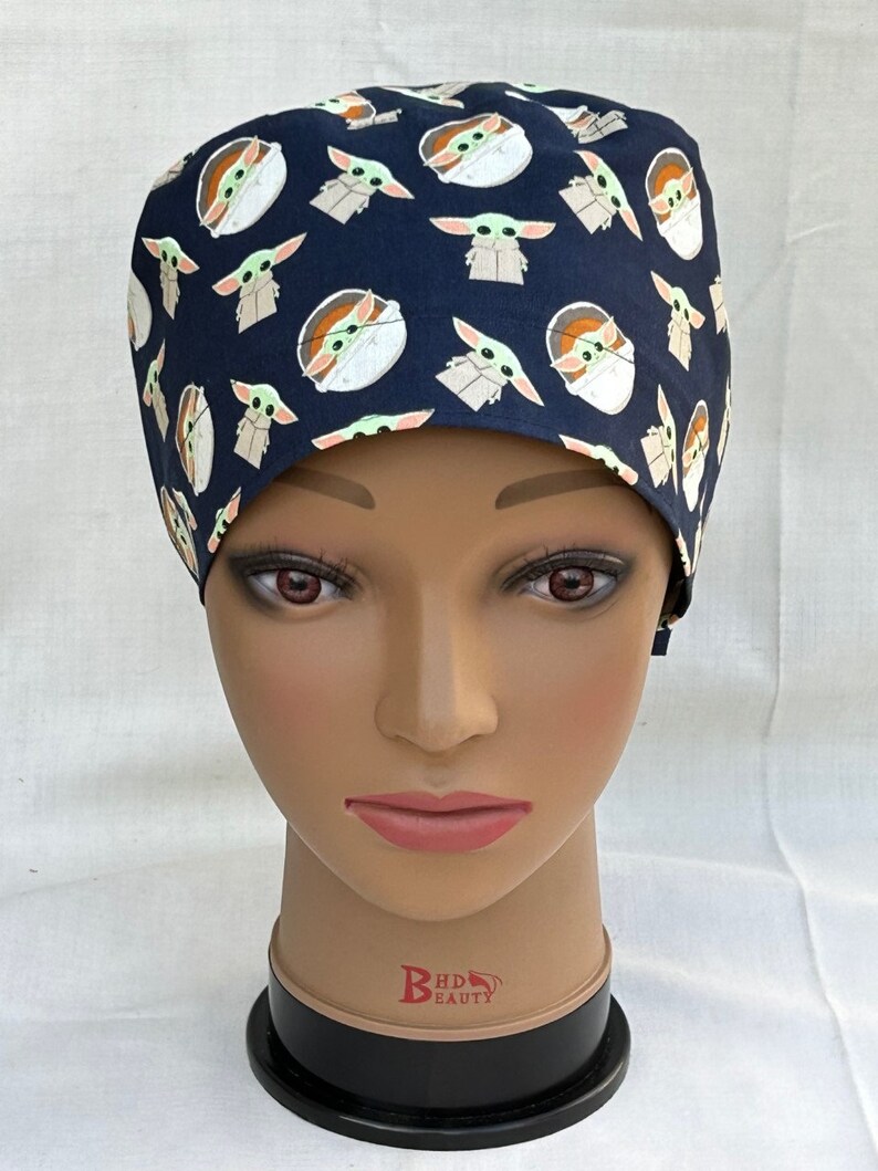 May include: A dark blue scrub hat with a repeating pattern of small green alien characters. The hat is made of a soft, comfortable fabric and is perfect for healthcare professionals.