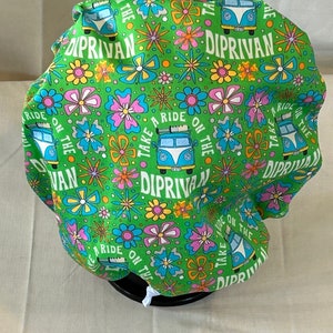 May include: Green fabric shower cap with a psychedelic pattern featuring flowers, stars, and a vintage van with the text "Take a Ride on the Van" and "Diprivan".