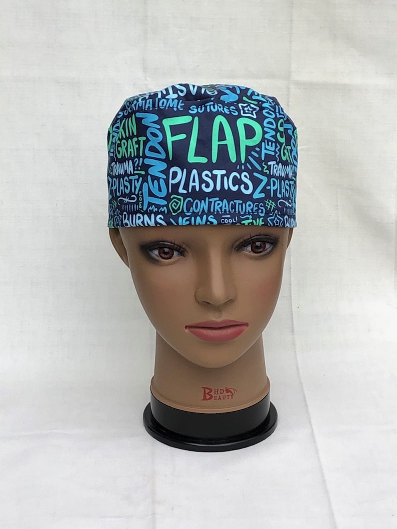 May include: A blue and green surgical scrub hat with a variety of medical terms printed on it, including "FLAP", "PLASTICS", and "CONTRACTURES".