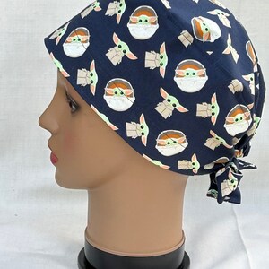 May include: A blue surgical scrub hat with a repeating pattern of a green alien character in a pod. The hat has a tie at the back.