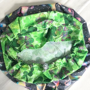 May include: A green fabric with a shamrock pattern, the fabric is gathered around a white elastic band. The fabric is folded in half and the shamrock pattern is visible on both sides.