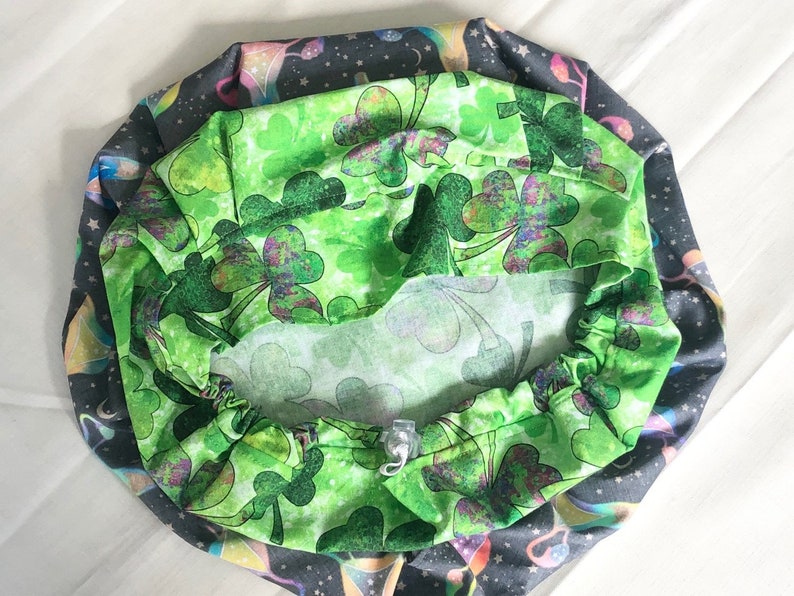 May include: A green fabric with a shamrock pattern, the fabric is gathered around a white elastic band. The fabric is folded in half and the shamrock pattern is visible on both sides.