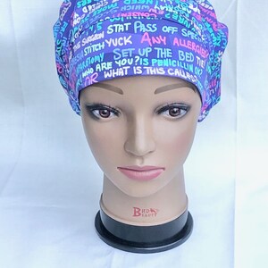 May include: A purple and blue surgical scrub hat with a variety of text printed on it, including "STAT PASS OFF SPECI", "HUPAROTOMY SET UP THE BED TIE", "SIA STITCH YUCK ANY ALLERGIES", "RIOR WHAT IS THIS CALLED?", "WHO ARE YOU? IS PENICILLIN OK", "CONSEN", "Sh", "ARE THOURL", "ESTER ARE", "EWWHICH Sco", "CHEED Y", "NEED Mel", "INSPLANTCALL HATE STAPLERS", "CAS", "0", "YERY VEST", "A".