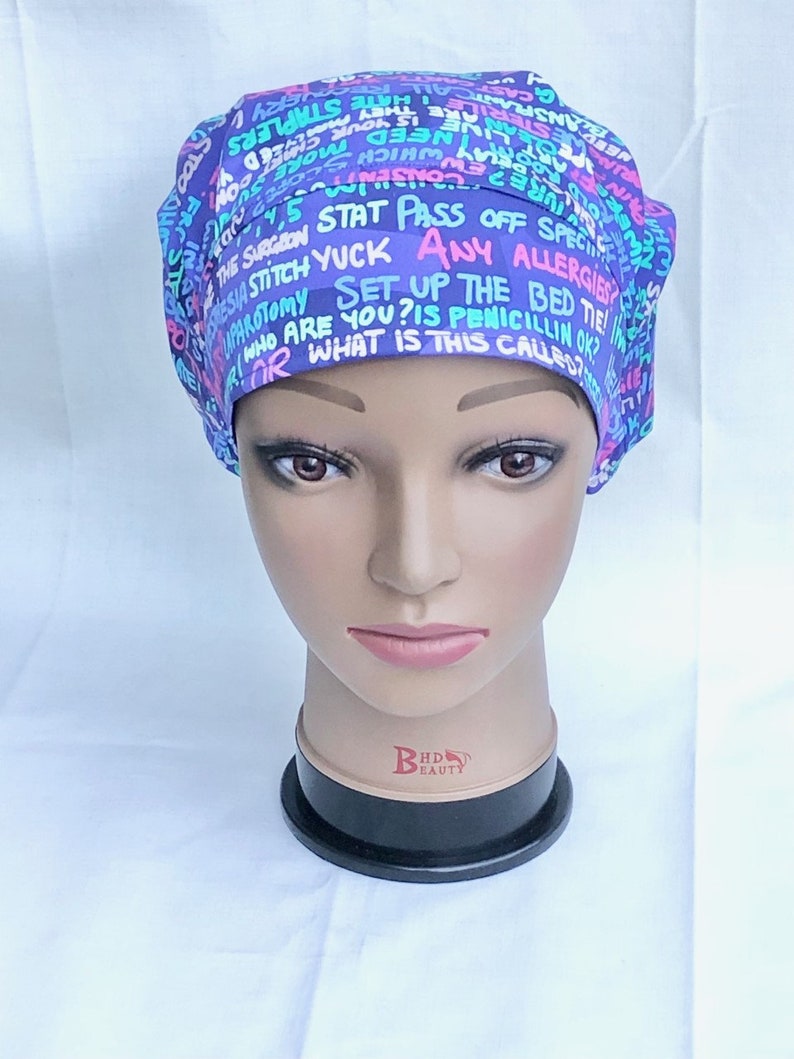 May include: A purple and blue surgical scrub hat with a variety of text printed on it, including "STAT PASS OFF SPECI", "HUPAROTOMY SET UP THE BED TIE", "SIA STITCH YUCK ANY ALLERGIES", "RIOR WHAT IS THIS CALLED?", "WHO ARE YOU? IS PENICILLIN OK", "CONSEN", "Sh", "ARE THOURL", "ESTER ARE", "EWWHICH Sco", "CHEED Y", "NEED Mel", "INSPLANTCALL HATE STAPLERS", "CAS", "0", "YERY VEST", "A".
