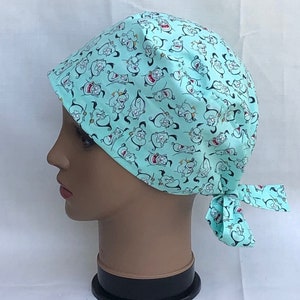 May include: A turquoise blue scrub hat with a repeating pattern of cartoon genie characters. The hat has a tie at the back.