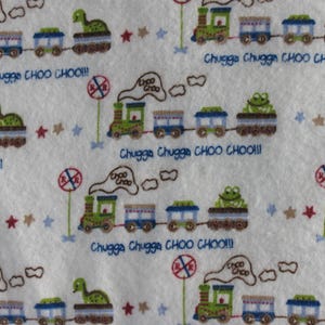 K&ouml;nnte beinhalten: Wei&szlig;er Stoff mit einem sich wiederholenden Muster aus gr&uuml;nen Z&uuml;gen, blauen Waggons und Tierfiguren. Der Text "Chugga Chugga CHOO CHOO!!!" ist in Blau geschrieben. Rote und blaue Sterne und Stoppschilder sind ebenfalls vorhanden.