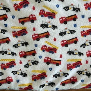 K&ouml;nnte beinhalten: Wei&szlig;er Stoff mit einem sich wiederholenden Muster aus roten Feuerwehrautos, schwarz-wei&szlig;en Polizeiautos, gelben Leitern, blauen Schilden und roten Hydranten. Geeignet f&uuml;r Kinderartikel.