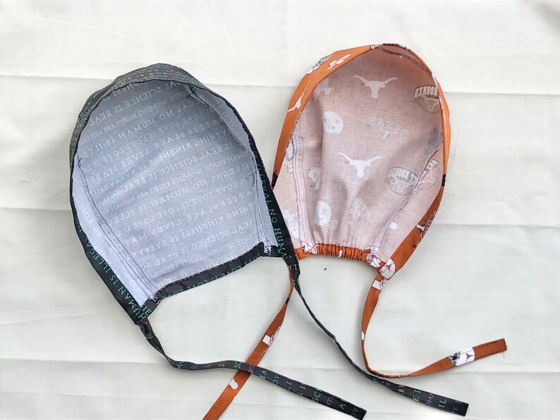 May include: Two fabric hats with ties. One hat is black with white text and the other is orange with white text and a white Longhorn steer logo.