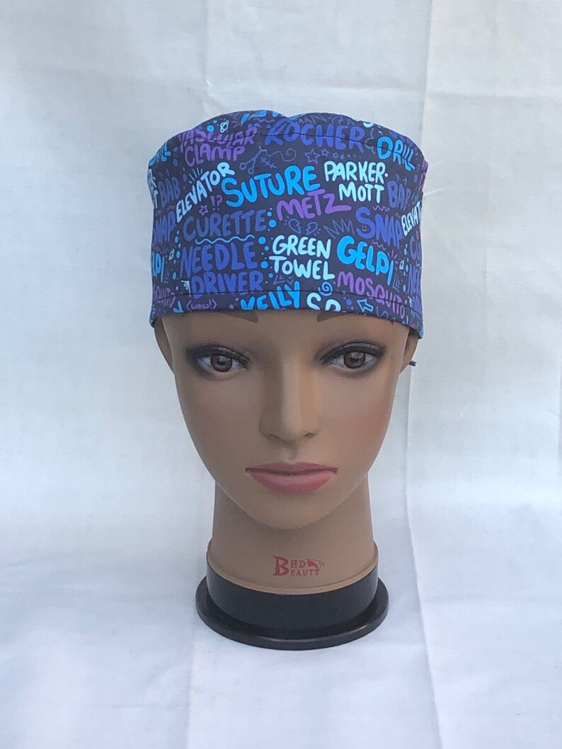 May include: A blue and purple surgical scrub hat with a variety of medical terms printed on it, including "Suture", "Parker", "Metz", "Mott", "Green Gel", "Driver", "Towel", and "Mosquito".