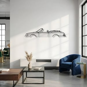 May include: A black metal wall art piece depicting the side profile silhouette of a convertible car. The design features clean, minimalist lines outlining the vehicle's body, including the windshield, door, and rear trunk area, mounted on a wall.