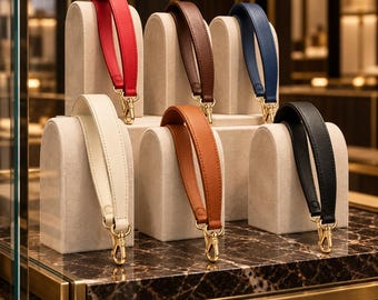 Op de afbeelding: Een collectie van zes polsbandjes in rood, donkerbruin, marineblauw, crème, tan en zwart. Elke band heeft een gladde afwerking, gestikte randen en een goudkleurige metalen karabijnhaak aan elk uiteinde voor een veilige bevestiging aan tassen.