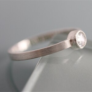 May include: A simple silver band ring with a single, small, round, clear gemstone set in a bezel setting.