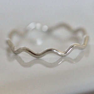 May include: A silver ring with a wavy design. The ring is simple and delicate.