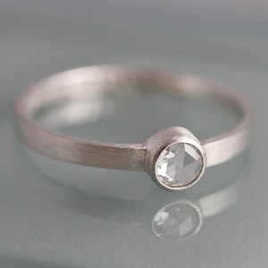May include: A silver ring with a round, clear gemstone set in a bezel setting.