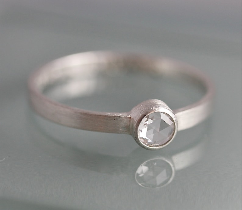 May include: A silver ring with a round, clear gemstone set in a bezel setting.