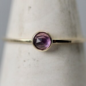 May include: A delicate gold ring with a round, faceted purple gemstone.