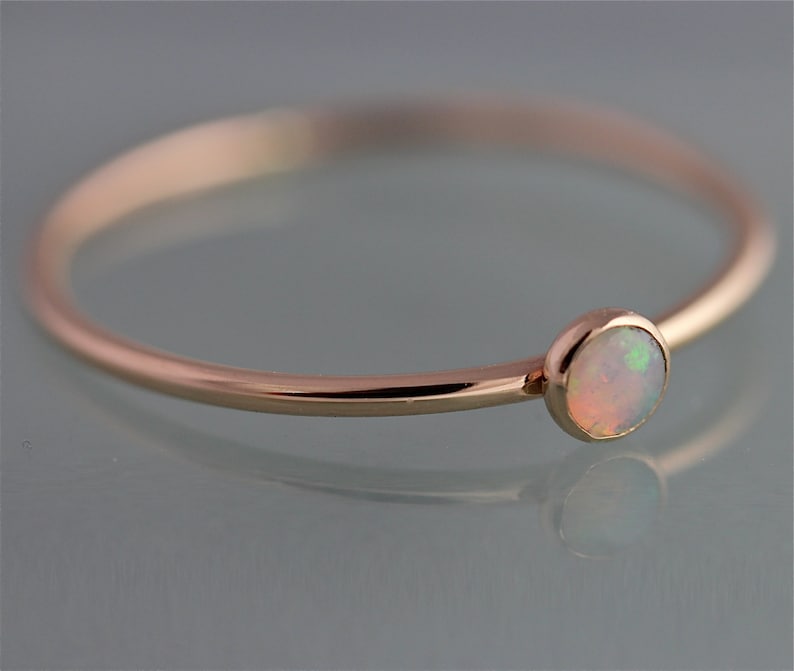May include: A delicate rose gold ring with a small, round opal gemstone.