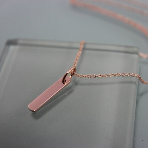 Puede incluir: Un collar de oro rosa con una cadena fina y un colgante rectangular largo.