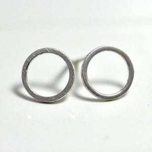 May include: A pair of silver circle stud earrings. The earrings are simple and minimalist, with a smooth, brushed finish.