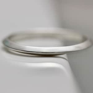 May include: A simple silver band ring with a slightly rounded edge.