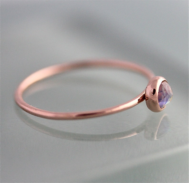 May include: A delicate rose gold ring with a small, round, iridescent gemstone.
