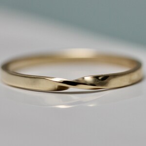 May include: A simple gold band ring with a twisted design.