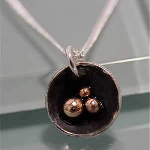 May include: A silver chain necklace with a round pendant. The pendant is black with three small, round, rose gold spheres inside.