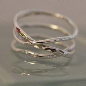May include: A silver ring with a twisted, interwoven design. The ring is made of smooth, polished metal and has a delicate, feminine look.