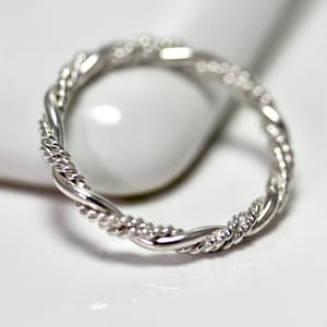 May include: A silver ring featuring a twisted rope design. The band is composed of two distinct strands, one smooth and polished, and the other textured with a fine, braided rope pattern that wraps around the entire circumference of the ring.