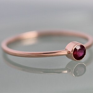 Op de afbeelding: Een delicate ring van ros&eacute;goud met een enkele, ronde robijn-edelsteen gezet in een bezel-setting.