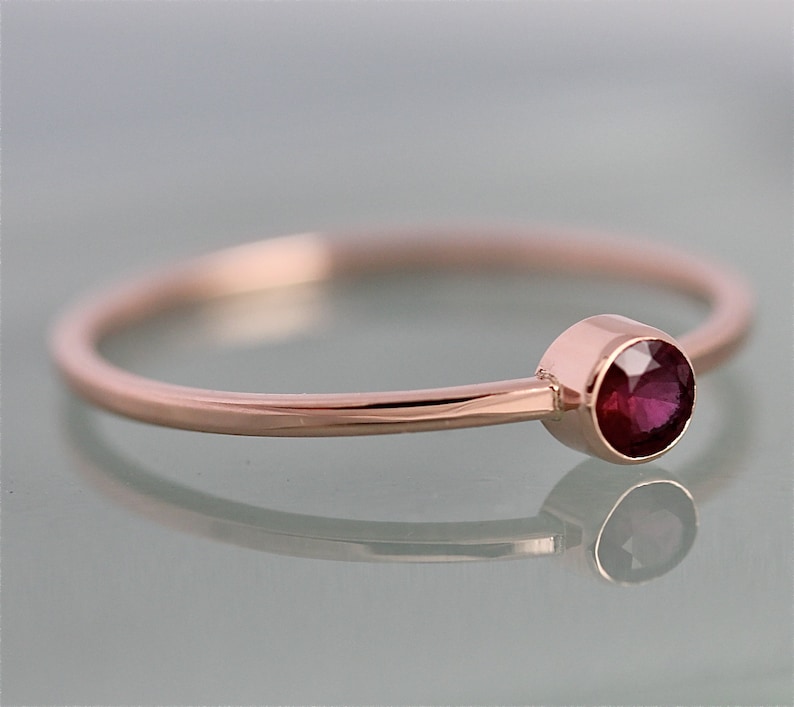Op de afbeelding: Een delicate ring van ros&eacute;goud met een enkele, ronde robijn-edelsteen gezet in een bezel-setting.