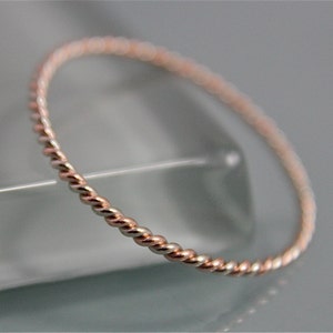May include: A thin, twisted, rose gold band ring.