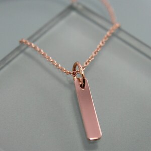 Puede incluir: Un collar de oro rosa con un colgante rectangular simple.