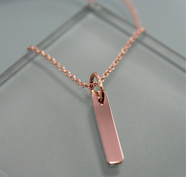 Puede incluir: Un collar de oro rosa con un colgante rectangular simple.