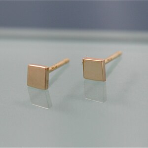 May include: A pair of gold square stud earrings. The earrings are small and simple, with a polished finish.