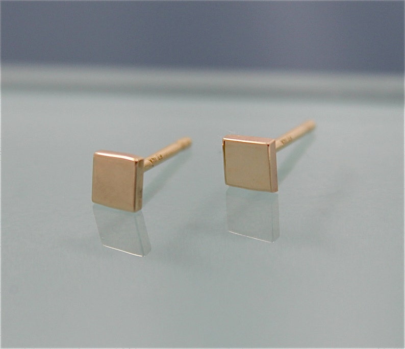 May include: A pair of gold square stud earrings. The earrings are small and simple, with a polished finish.