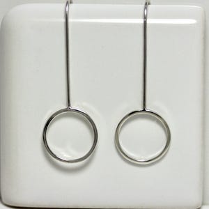 May include: A pair of silver dangle earrings with a simple circle design. The earrings are suspended from a thin silver wire.